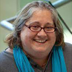A smiling woman with gray hair and glasses wearing a blue scarf.