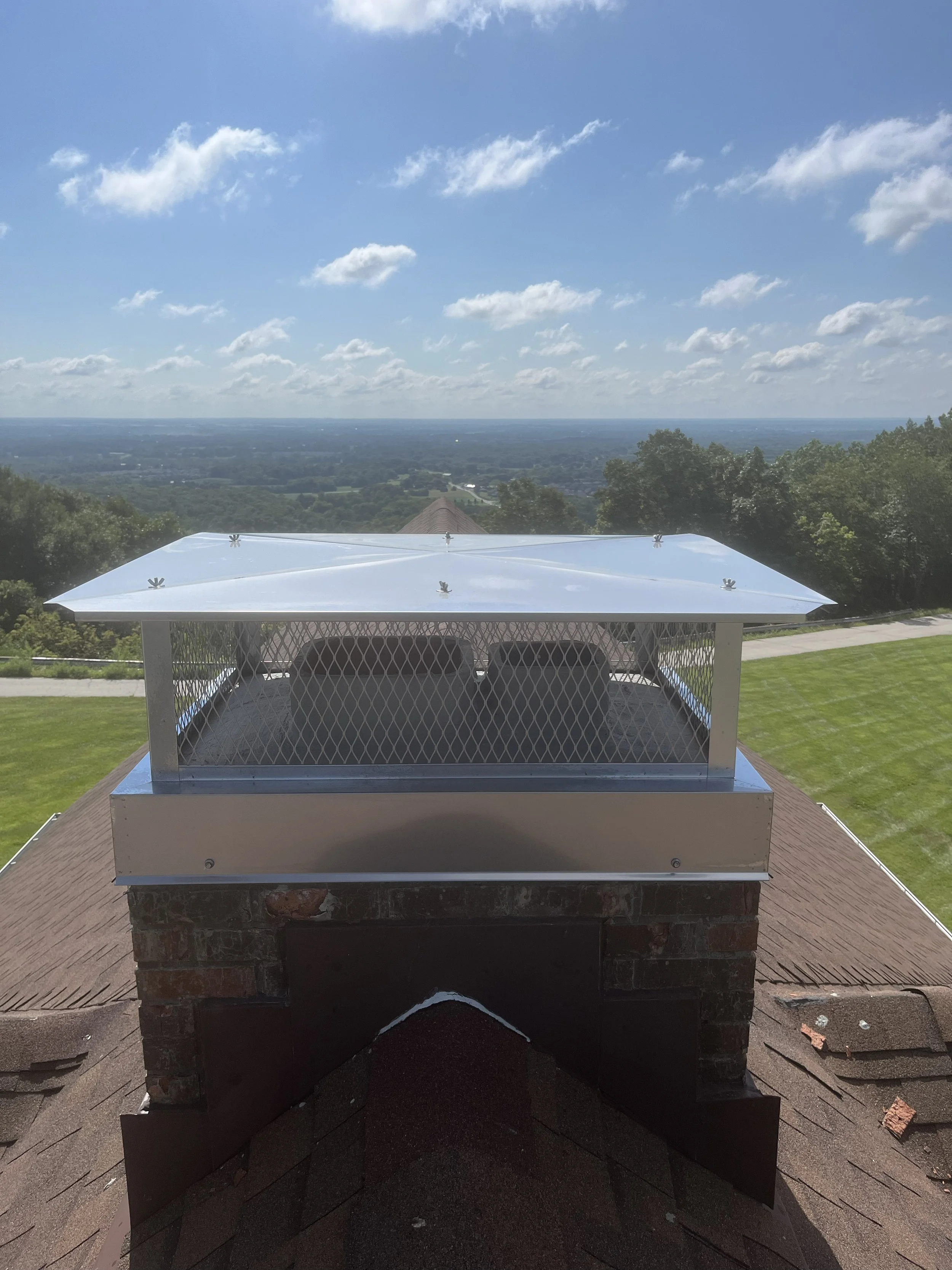 View of a large outdoor landscape with a blue sky and scattered clouds, seen from a rooftop with a metal vent at the foreground.