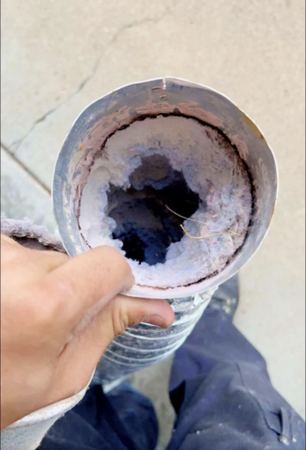 A person holding a plastic bottle with a burnt and charred interior, indicating it was used to burn something. The bottle appears to have some residue inside and is being held in front of a sidewalk.