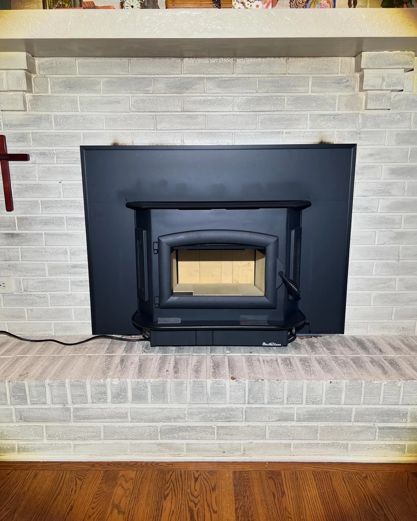 A gas fireplace with a black metal surround installed in front of a white brick wall, situated on a brick hearth with a wood floor in front.