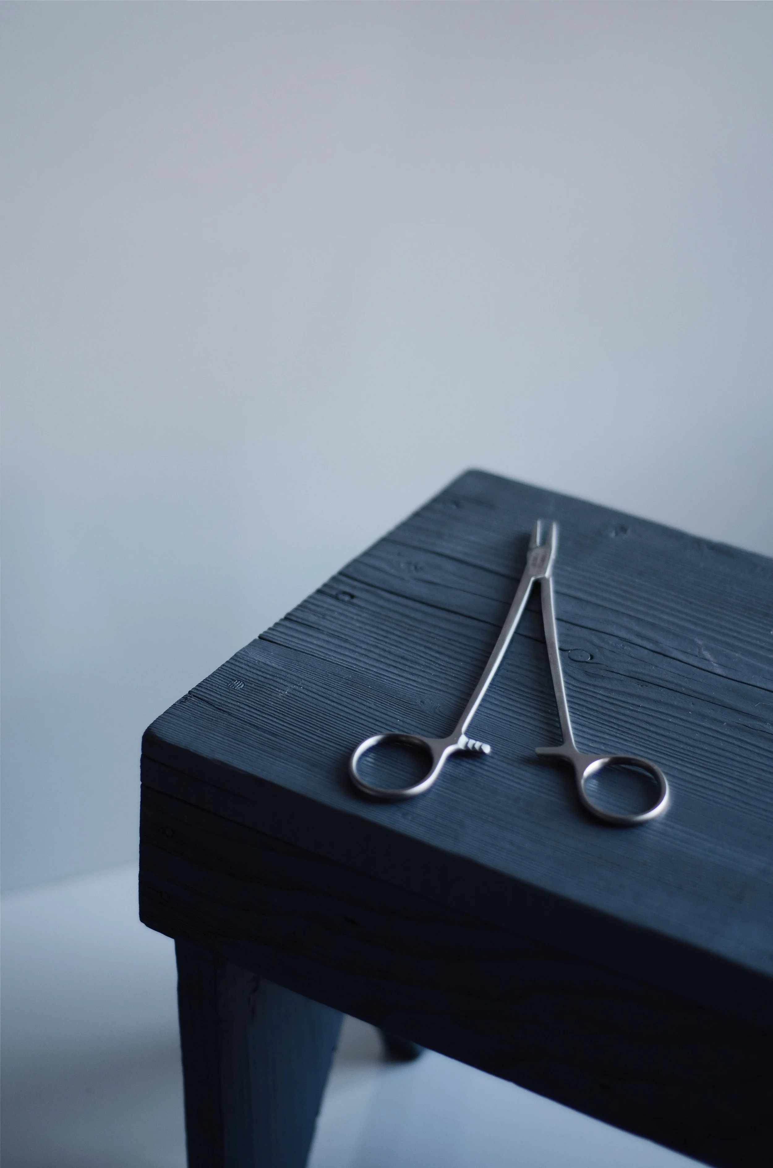 A pair of surgical scissors resting on a dark wooden table.