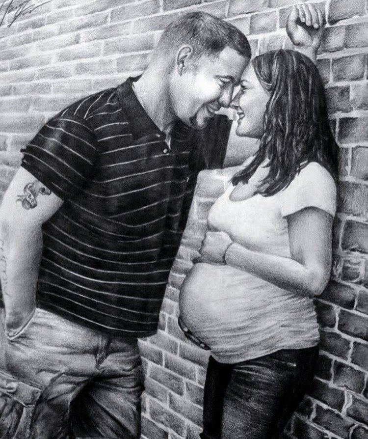 A black-and-white photo of a man and a pregnant woman leaning against a brick wall, smiling and touching foreheads.