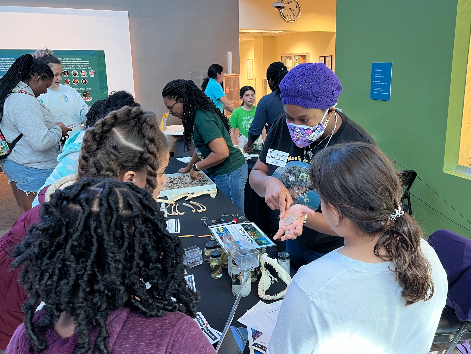 Dr. Adania Flemming sharing fish diversity and natural history science with community members during BlackInNHMs Week, holding a small ray beside a hands-on “fish vs. fishes” activity.