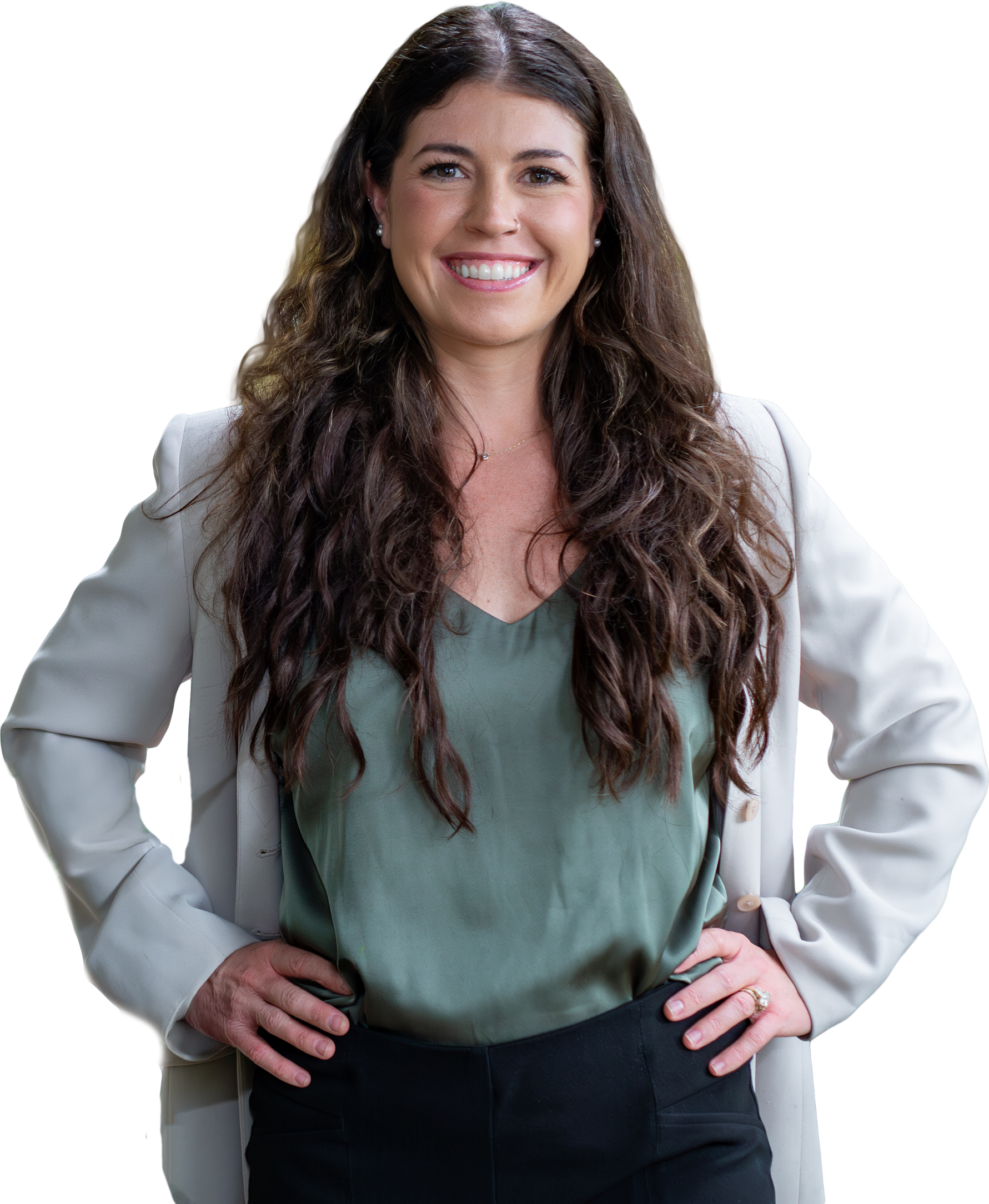 A woman with long, wavy brown hair smiling confidently, wearing a white blazer over a green blouse, with hands on hips, standing against a background with a red shape.