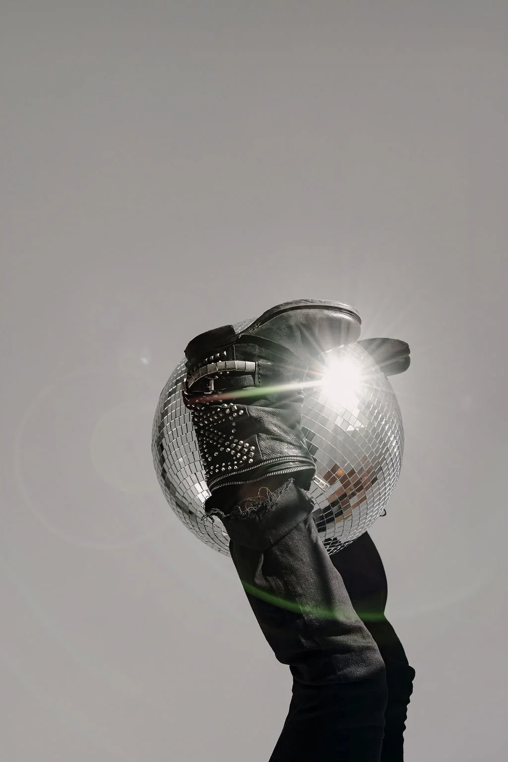 Person wearing black gloves and ripped jeans holding a disco ball with the sun reflecting off of it in a clear sky