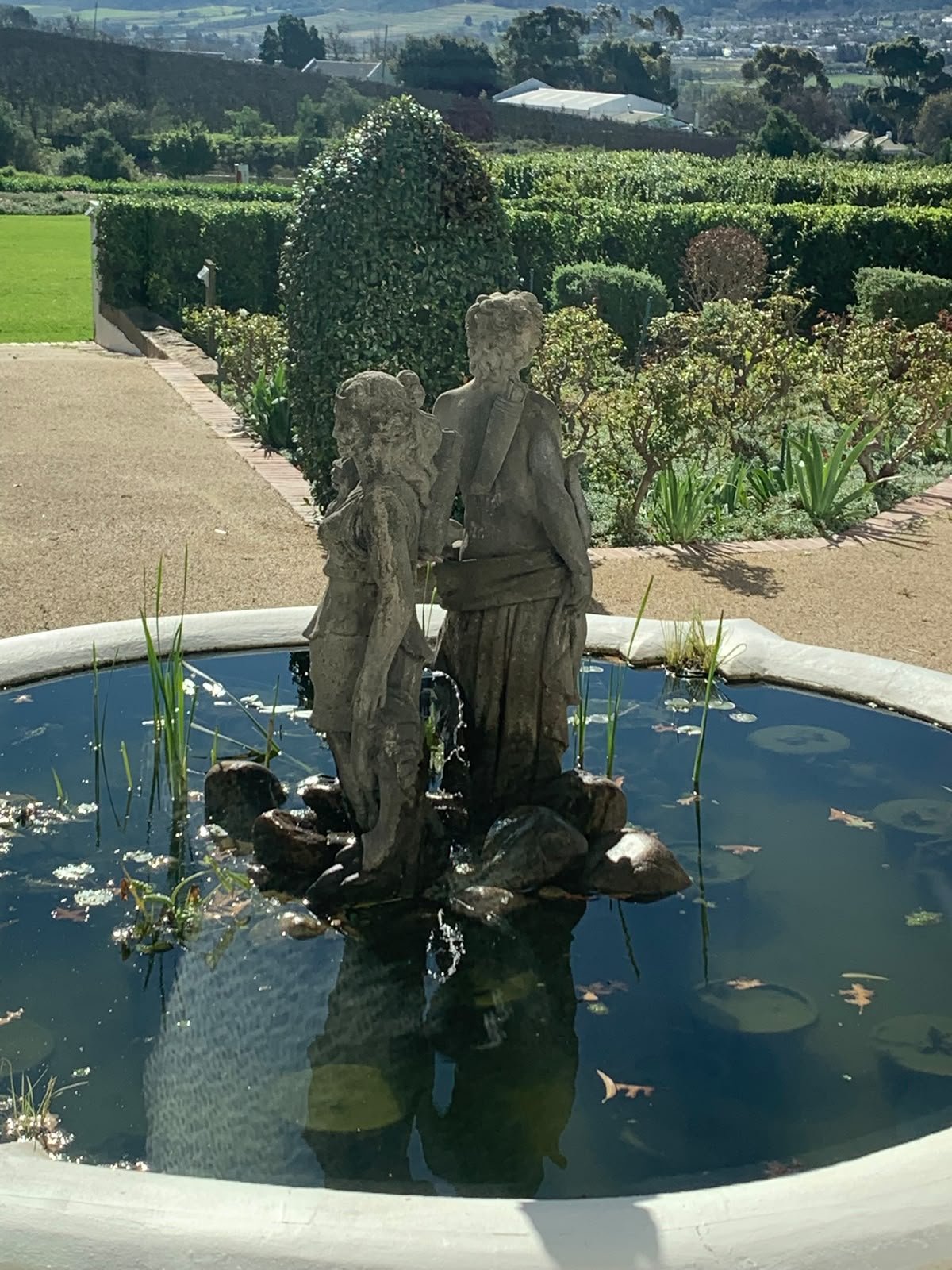 Statue of two children in a fountain with landscaped garden and countryside in the background.