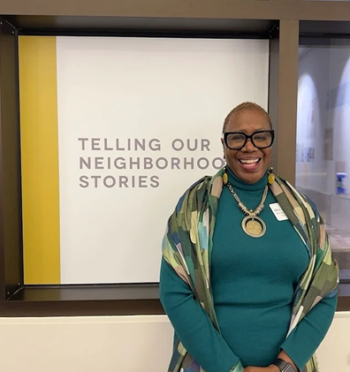 Reverend Dr. Odell Montgomery Cooper smiling and standing in front of a sign that reads 'Telling Our Neighborhood Stories'