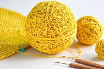 Two yellow decorative yarn balls, a yellow knitted item, and two yarn needles with wooden handles.