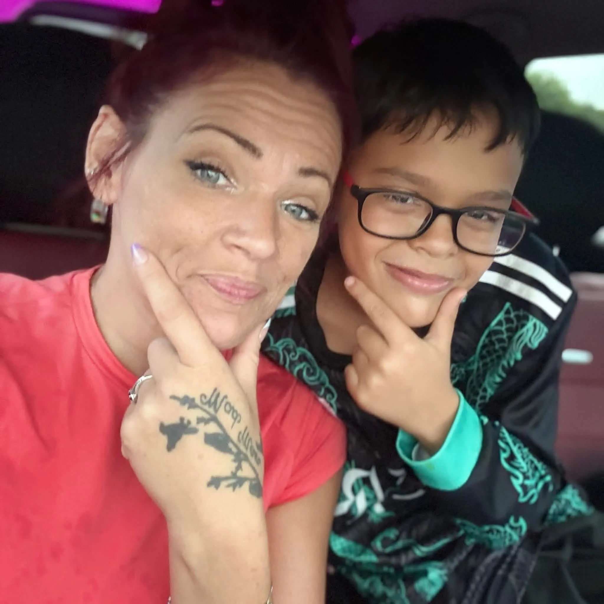 Close-up of two people, a woman and a young boy, smiling and making peace signs with their fingers.