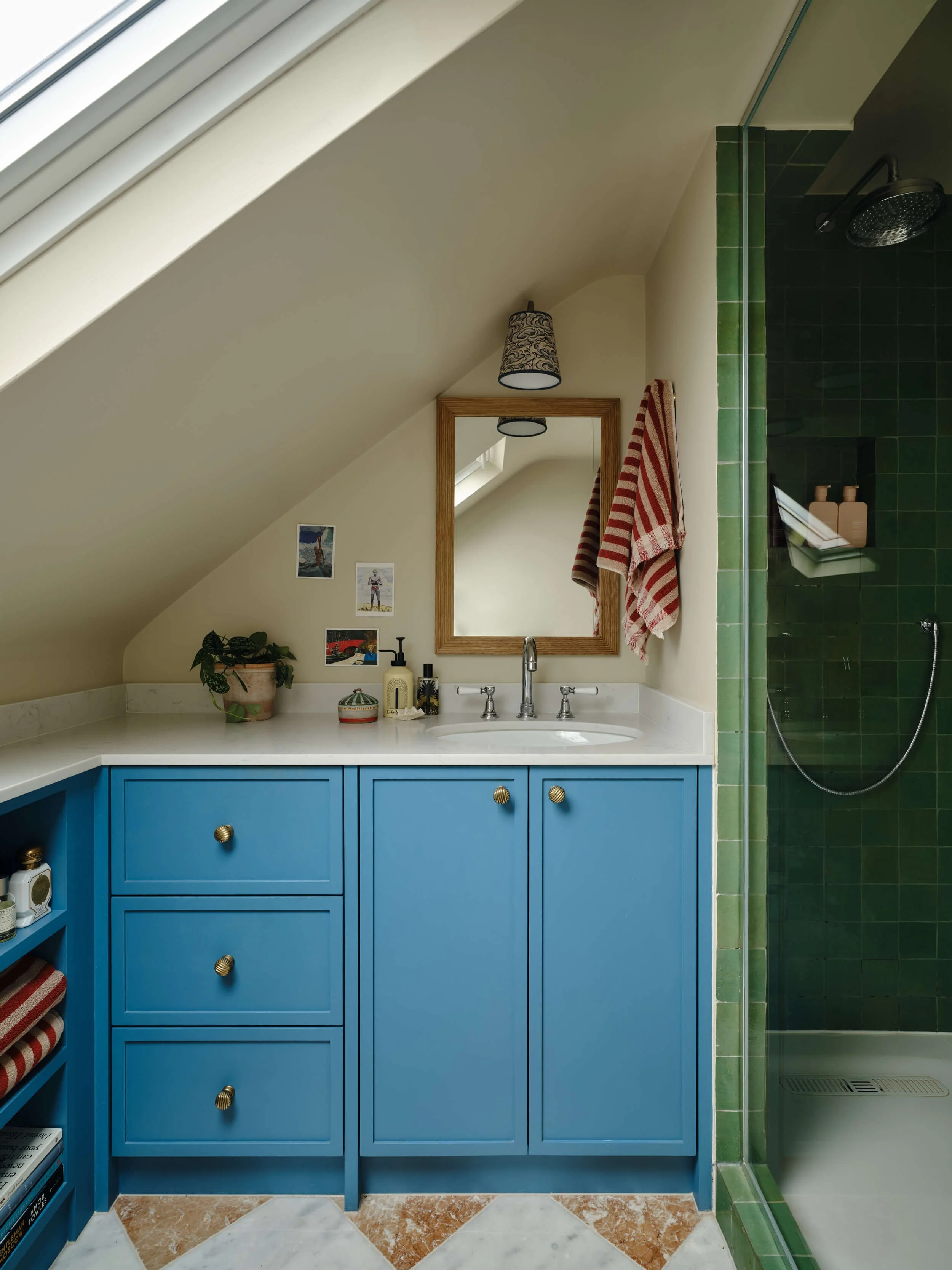 Loft bathroom with a sloped ceiling, blue vanity unit and a shower with green tiled walls.