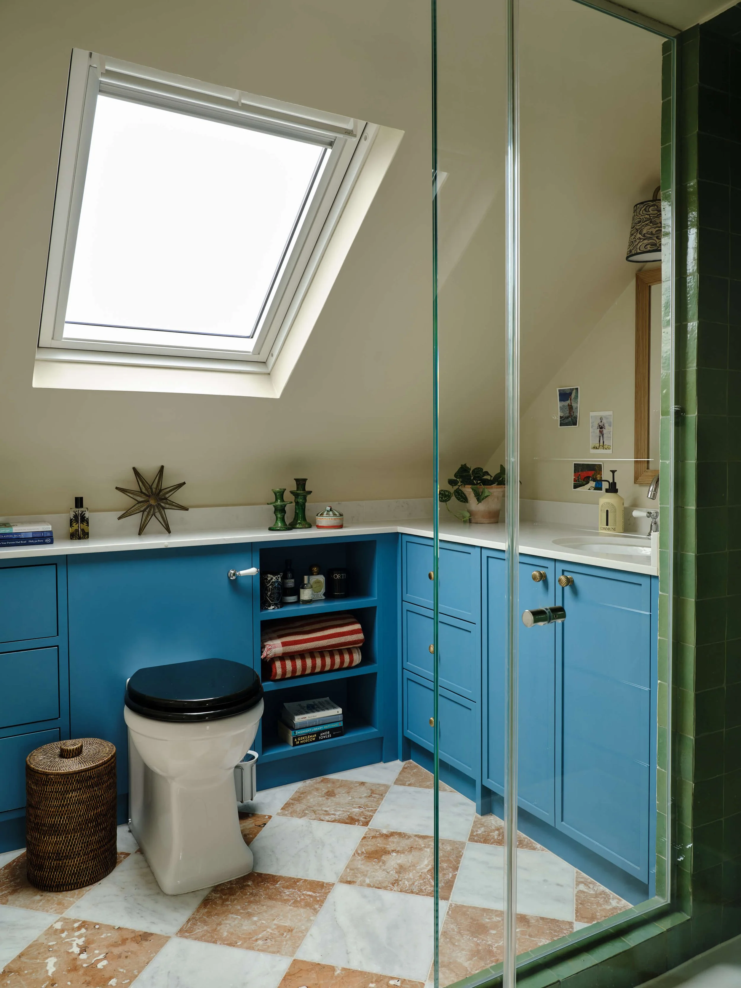 Loft bathroom with a skylight, blue cabinetry, green tiled shower and a patterned tiled floor.