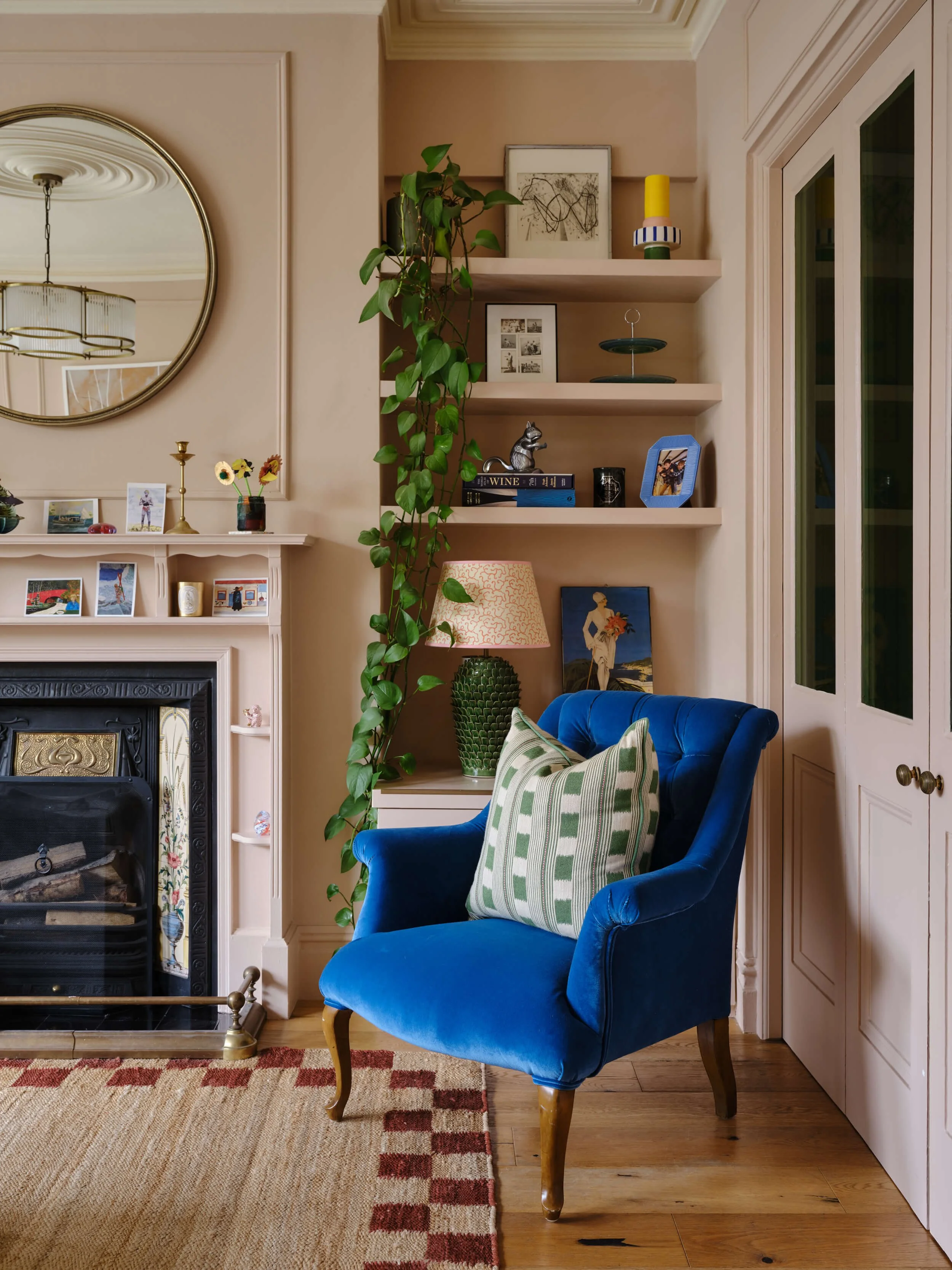 Living room corner with a bright blue armchair, white fireplace, built-in shelving and a patterned rug on wooden floors.