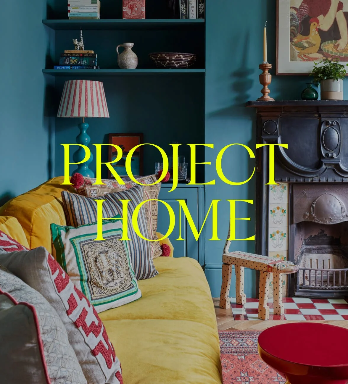 Colorful living room with yellow sofa, patterned pillows, a teal wall with bookshelf and a lamp, vintage fireplace, and a small wooden stool, with the text "PROJECT HOME" overlayed in yellow.