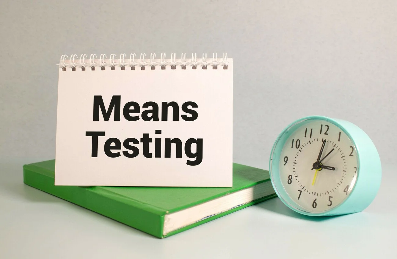 On a white background, a a sign says ' Means Testing' on top of a green book, next to a small blue clock.