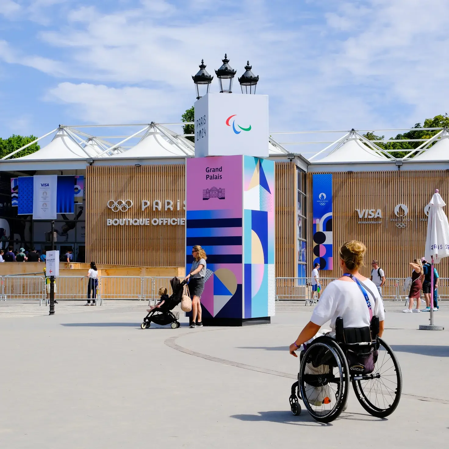 A wheelchair user facing away away from the camera and looking at other people walking around a square.