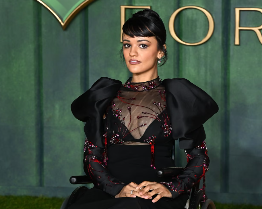 A woman (Marrissa Bode) is wearing a blacklong-sleeved dress, and is looking at the camera.