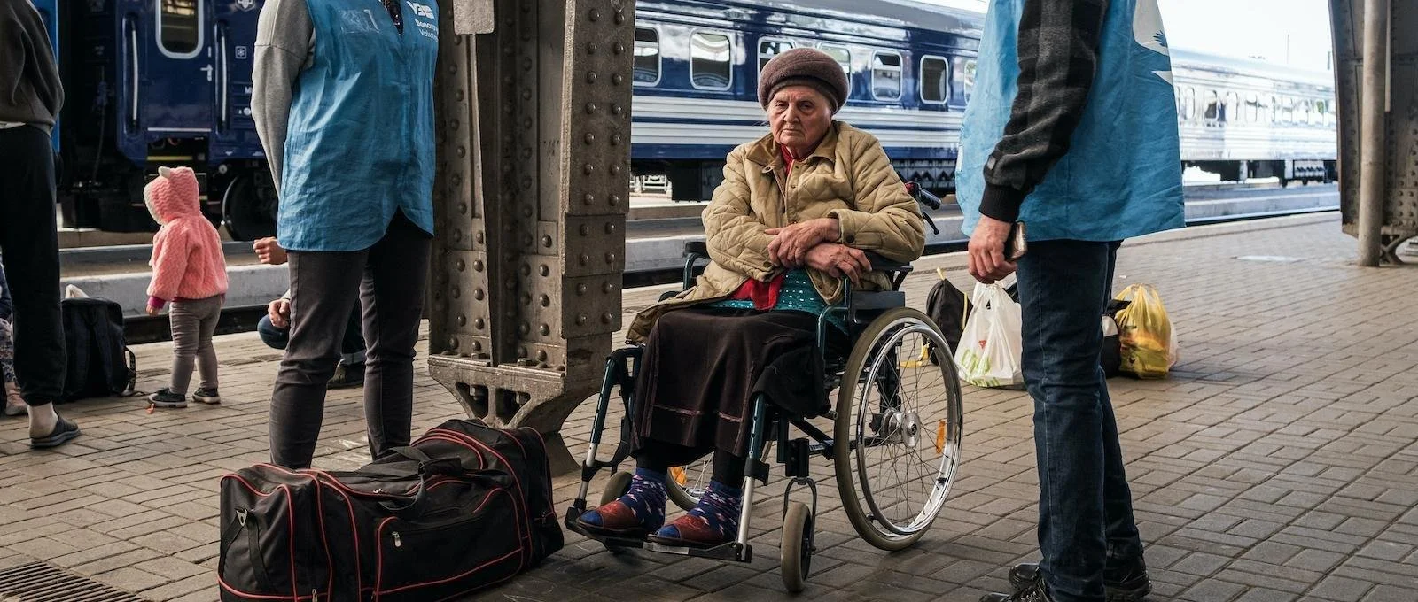 A elderly woman sitting in a manual wheelchair on a train platform