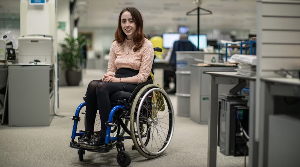 A woman (Niamh Ní Hoireabhaird) sitting in her wheelchair, in an office.