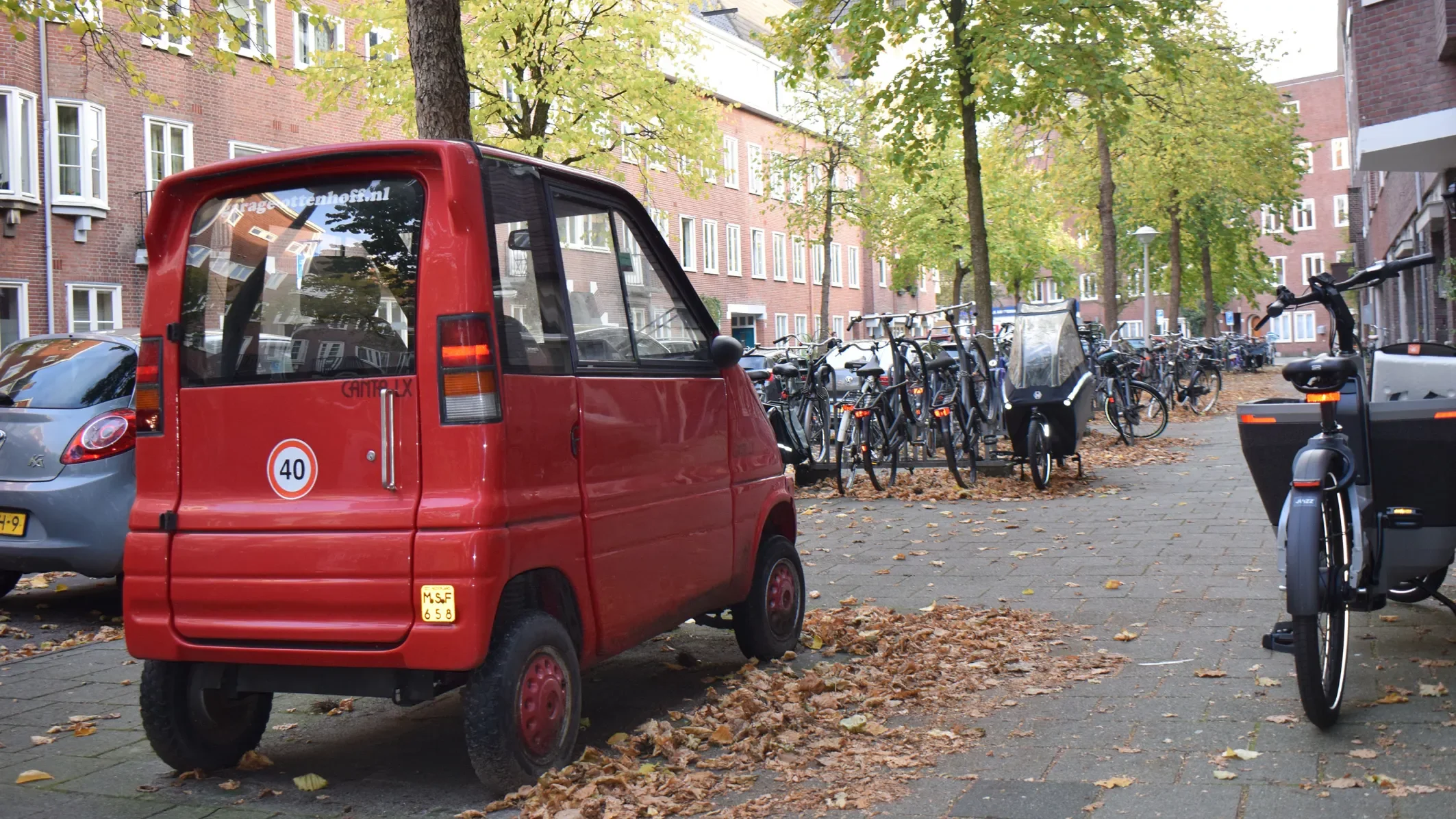 A small red car on a street full of bikes.