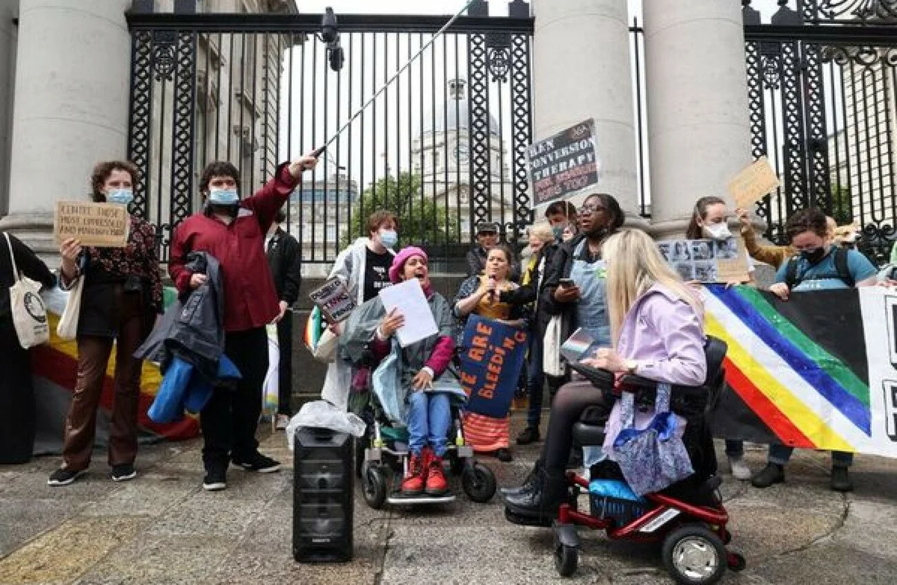 A large group of people protesting outside big blck gates.