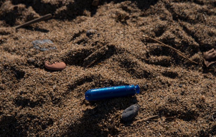 A blue platic tampon applicator on a bed of sand.