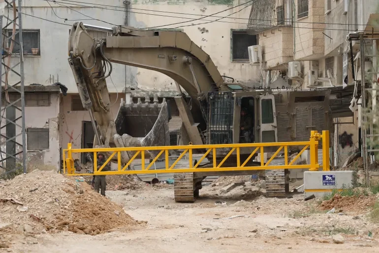 A digger in front of a mound of dirt and a yellow barrier.