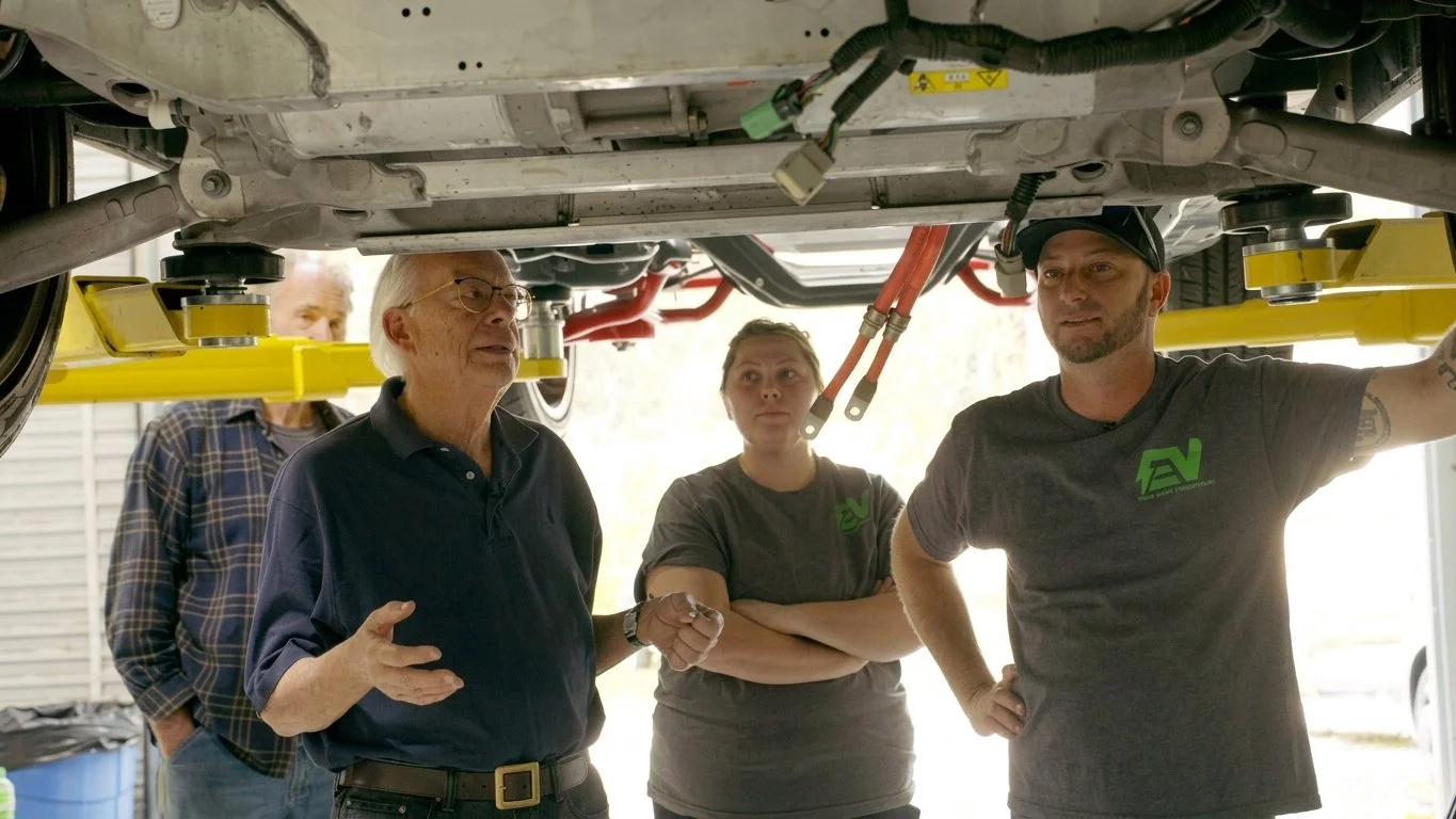 Green Shed staff discussing restoration under a car that is on a lift.