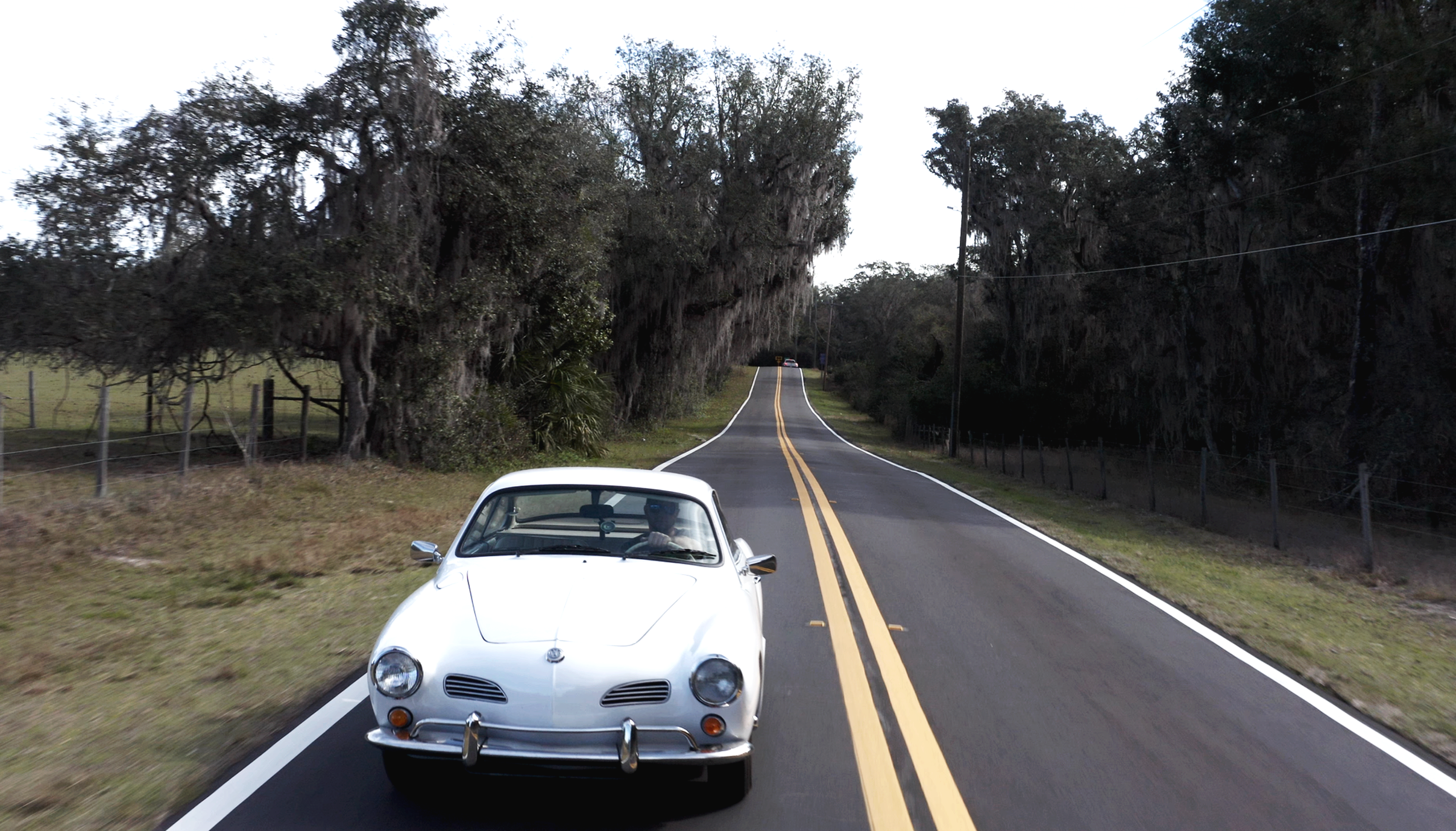 White classic convertible driving along a country road.