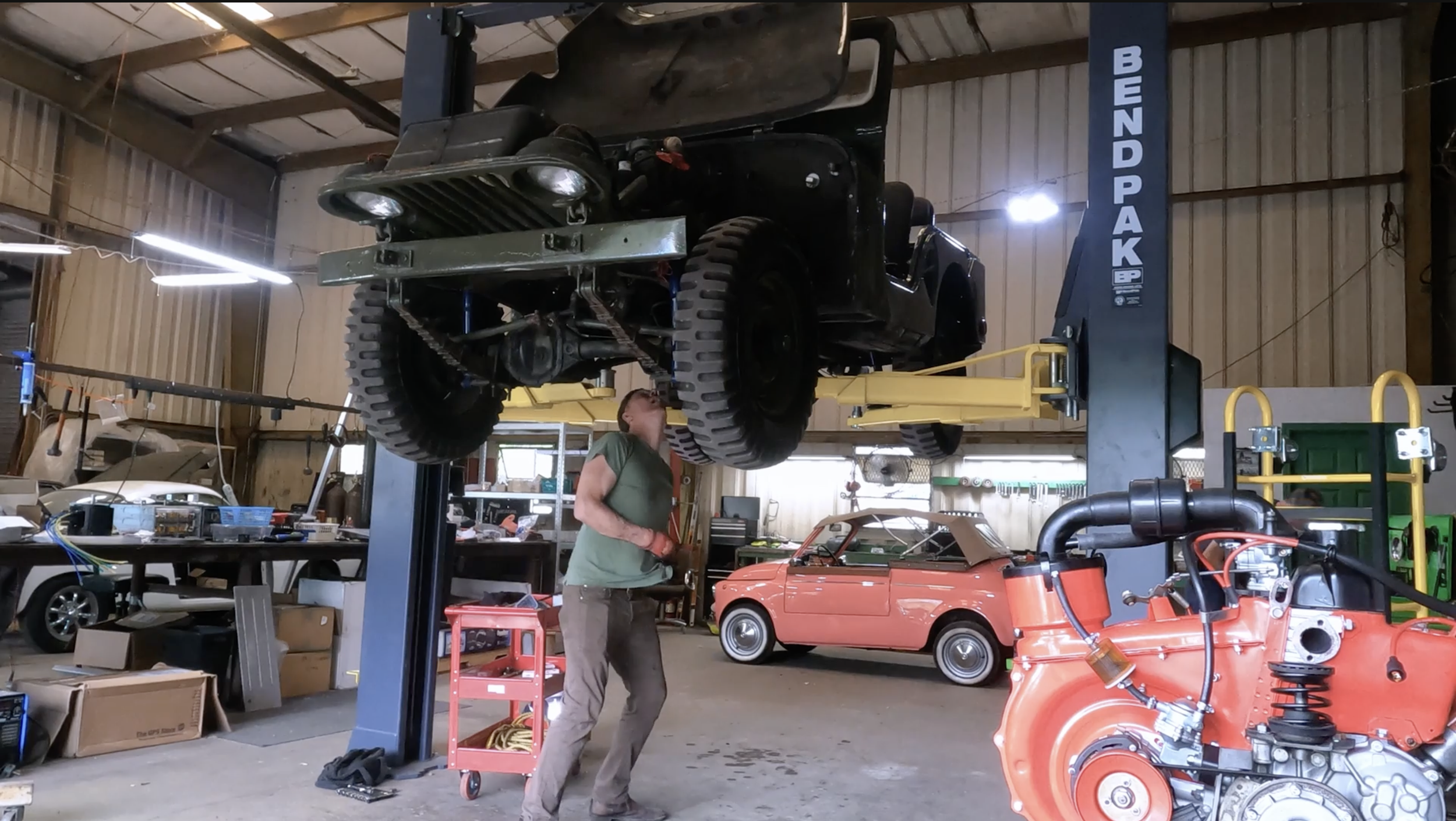 Technician working beneath a vintage Willys Jeep raised on a lift at Green Shed Conversions.