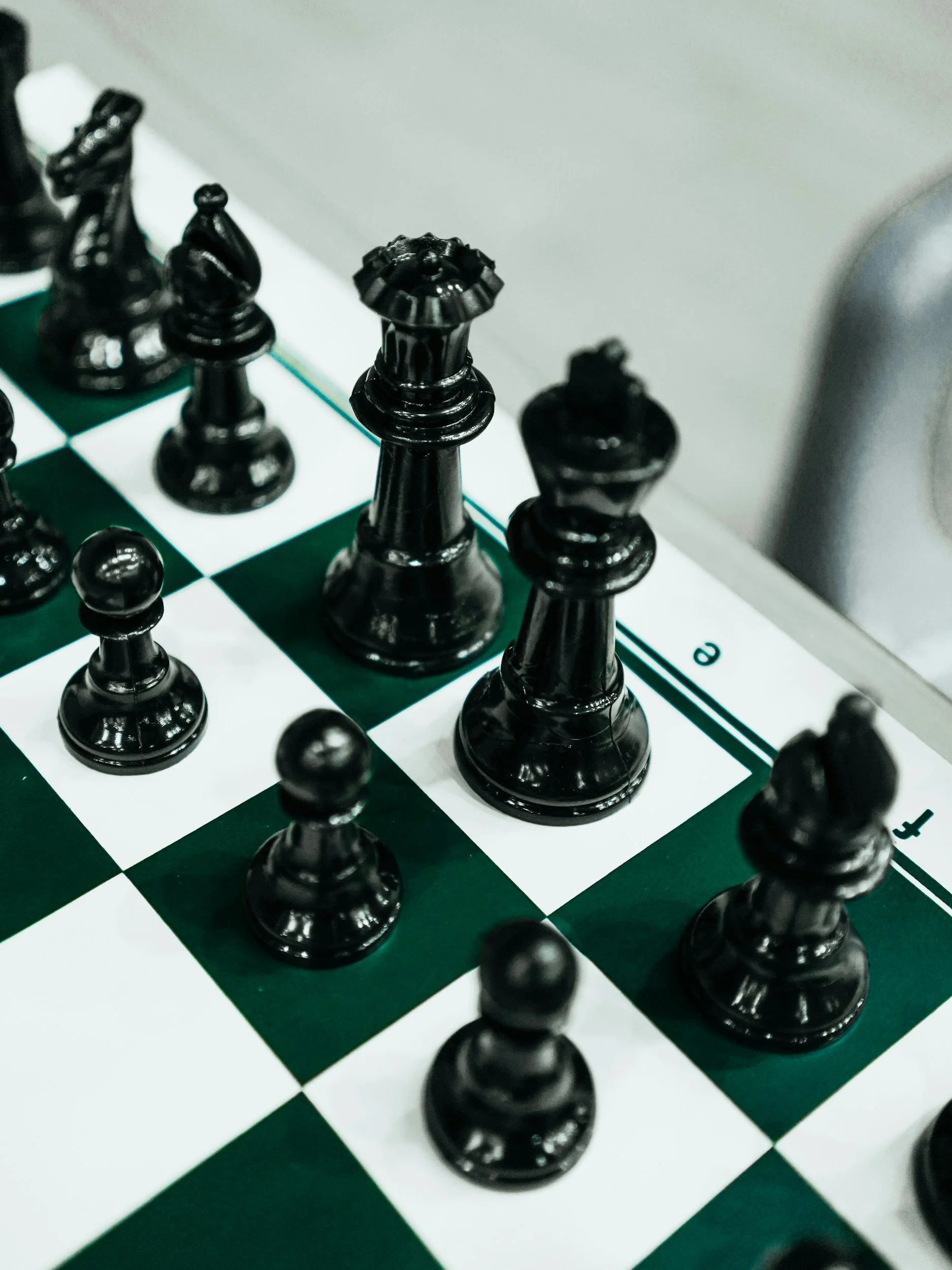 Black chess pieces on a green and white chessboard, with the focus on the king and queen in the foreground.
