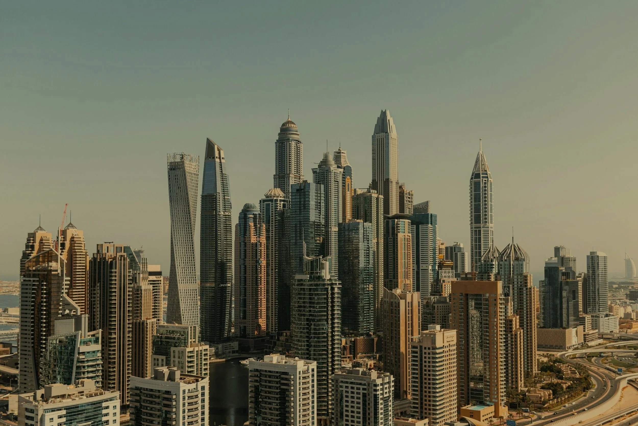 Skyline of a modern city with tall skyscrapers and buildings, including the Burj Khalifa, under a clear sky.