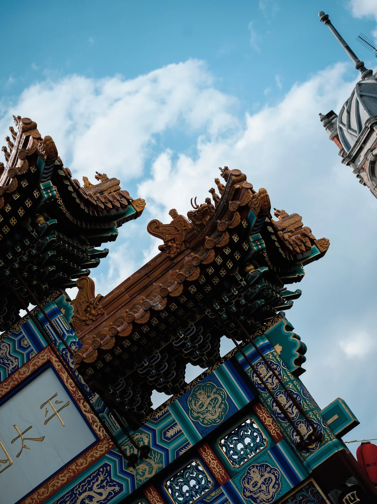 Close-up of ornate, colorful traditional Asian temple roof decorations with intricate gold, blue, and red patterns, set against a partly cloudy sky.