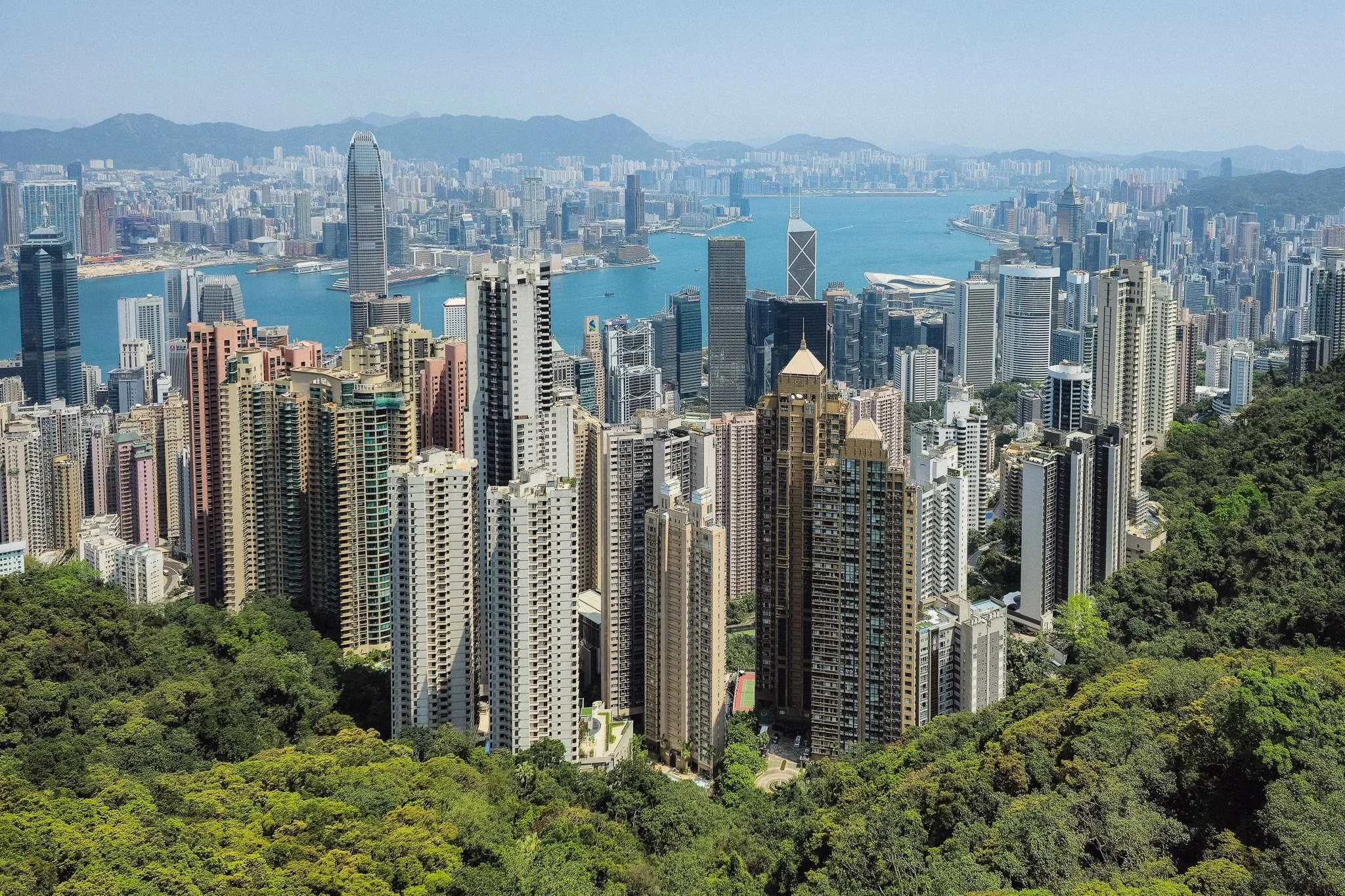 A city skyline with numerous tall buildings, a river running through the city, and a backdrop of mountains in the distance.