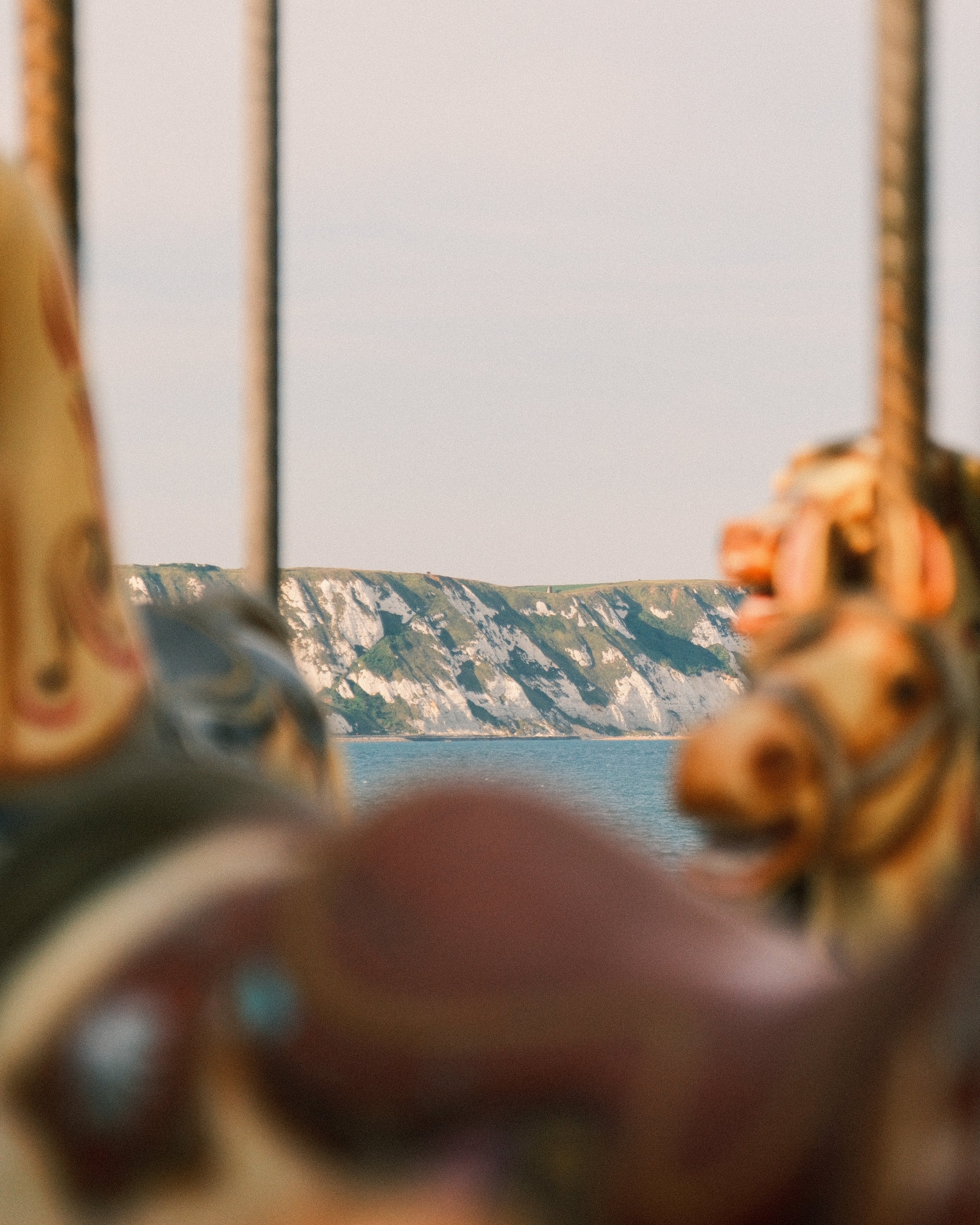 Blurry photo of a landscape with cliffs and water, seen through a window or frame, with some objects in the foreground.