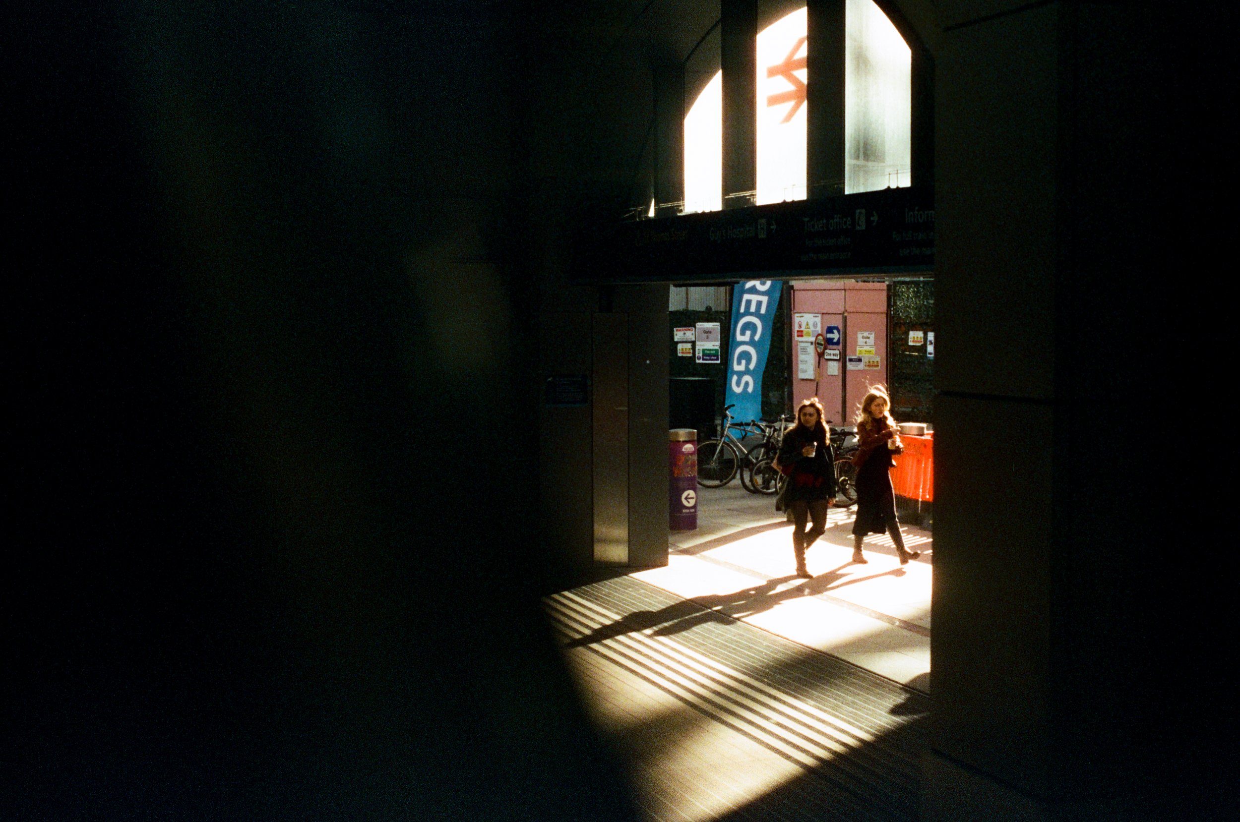 People walking through an airport terminal, with sunlight streaming into the darkened corridor.