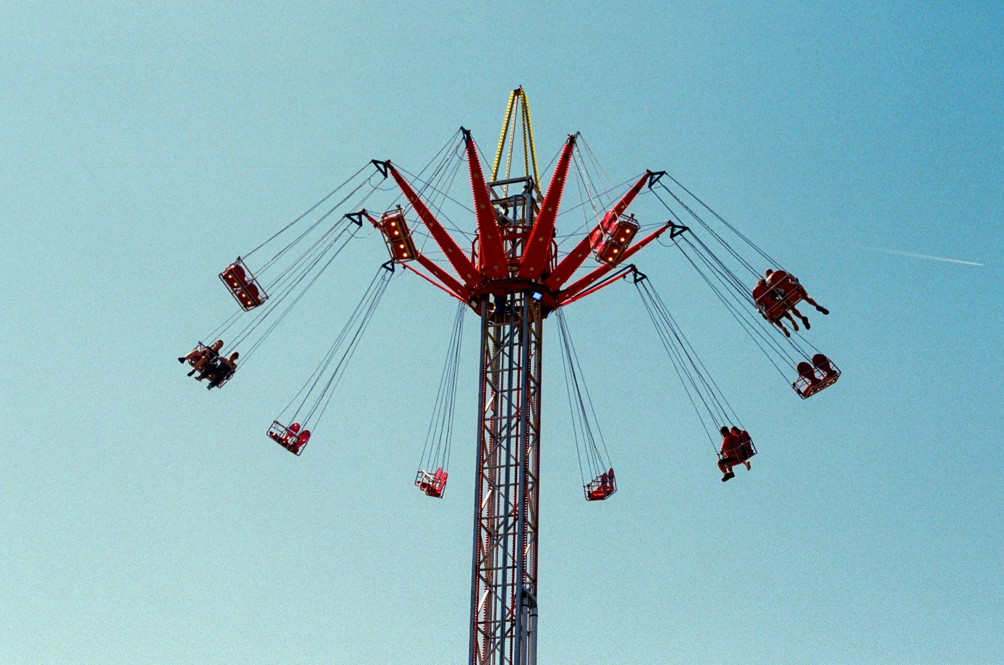 A tall red and yellow amusement park swing ride with people riding in swings, against a clear blue sky.