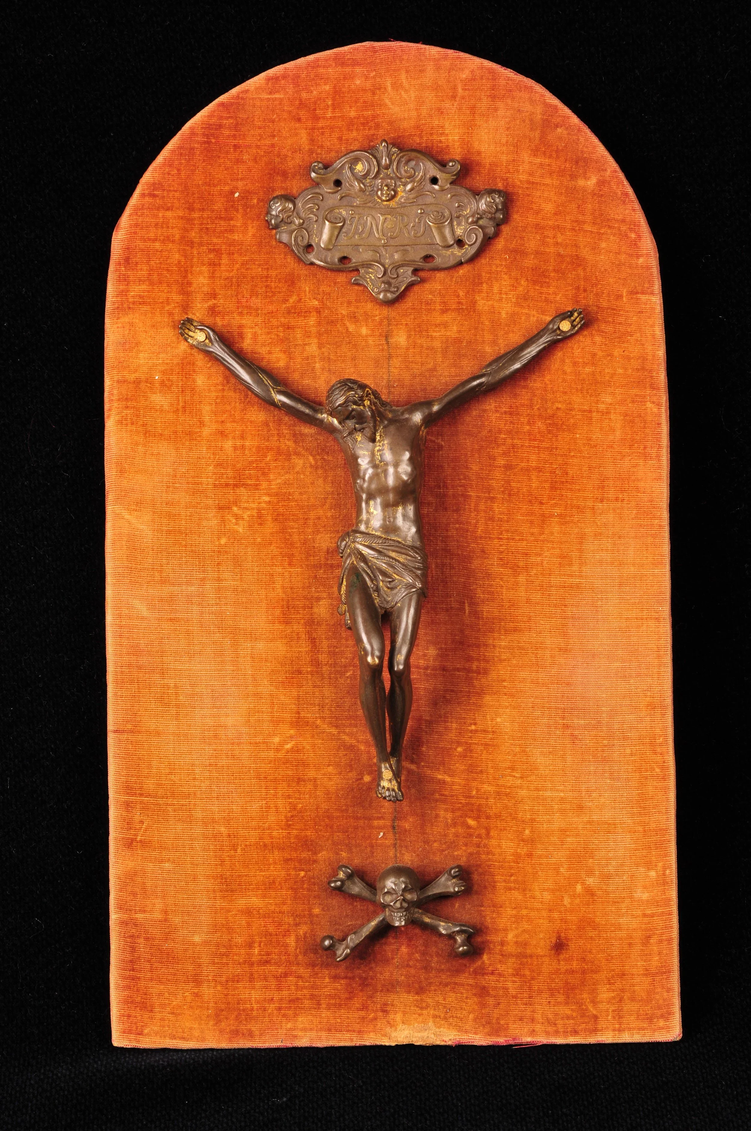 Carved crucifix mounted on an arched panel covered in faded orange velvet