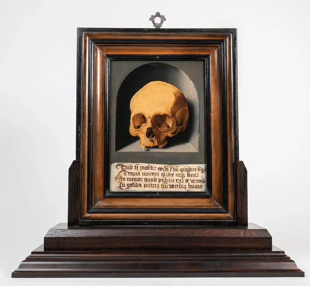 Human skull displayed in a carved wooden frame above a Latin inscription