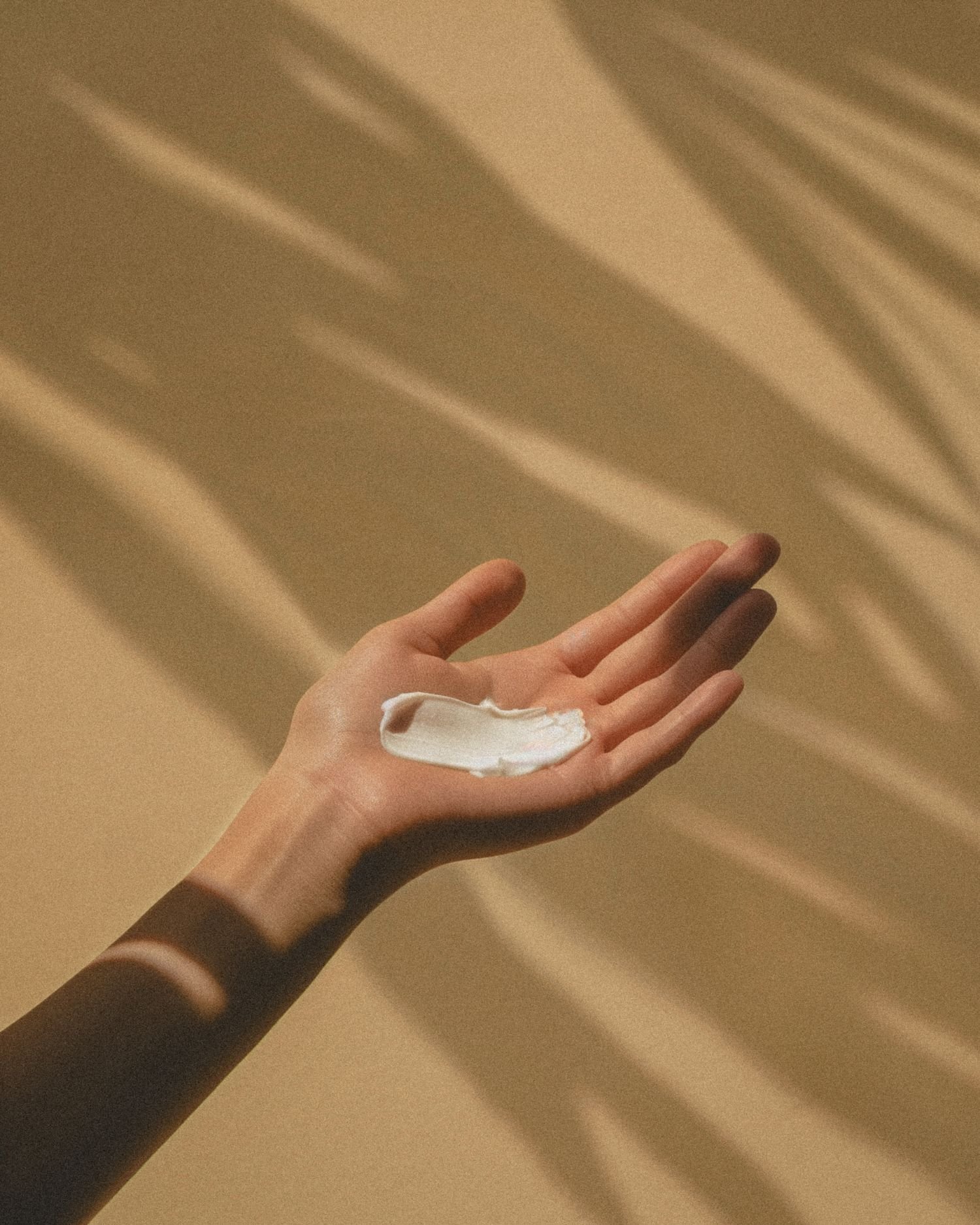 A hand holding a dollop of white cream, with a shadowed background.