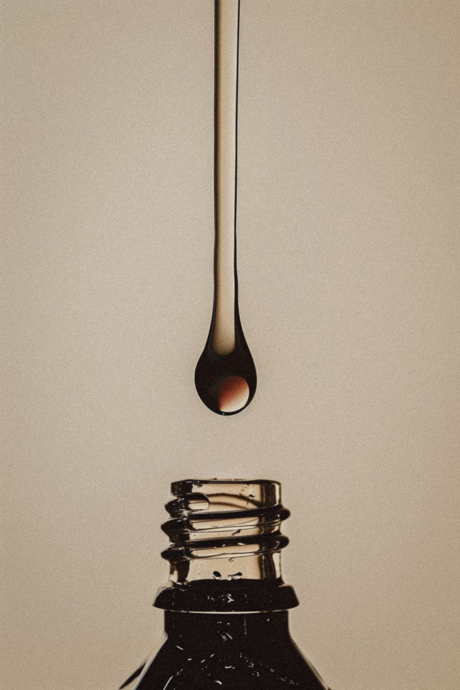 Close-up of a lightbulb with a single droplet of liquid hanging from the filament, in front of a beige background.