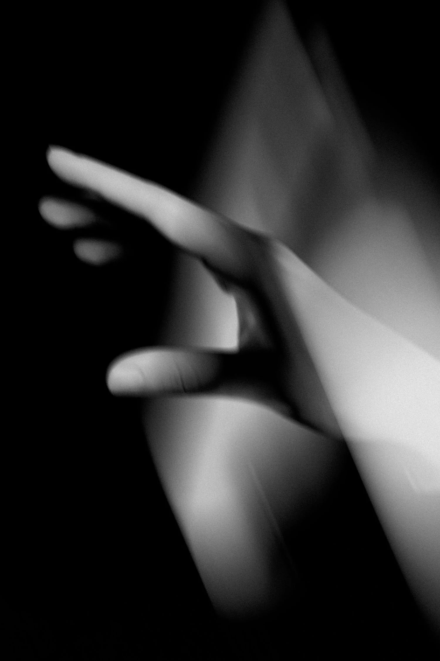 Black and white photograph of a person's hand with fingers raised near the face, creating a shadowy, abstract effect.
