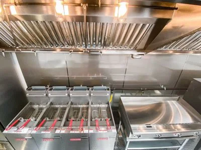 Industrial kitchen with stainless steel equipment, including deep fryers and a flat cooking surface.
