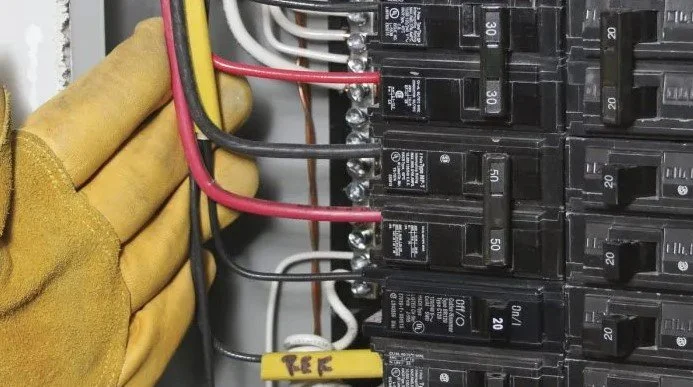 Close-up of an electrical electrical panel with circuit breakers and wires, with a gloved hand adjusting the wires.
