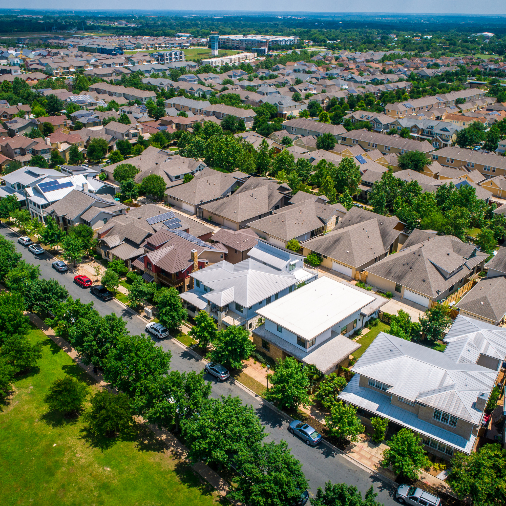 Aerial view of a residential neighborhood with multiple single-family houses, green trees, and parked cars along streets.