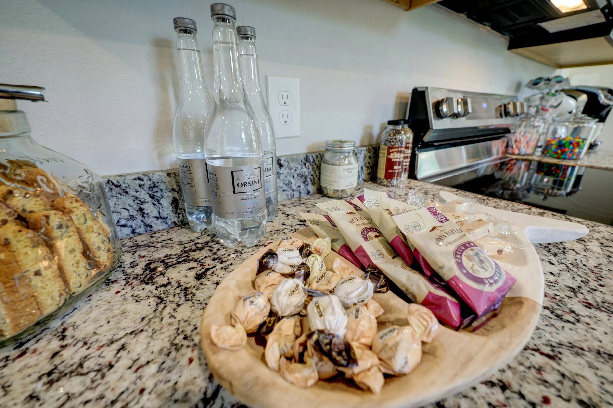 Granite kitchen counter with bottled mineral water, bread, wrapped chocolates, candy jars, and a coffee machine.
