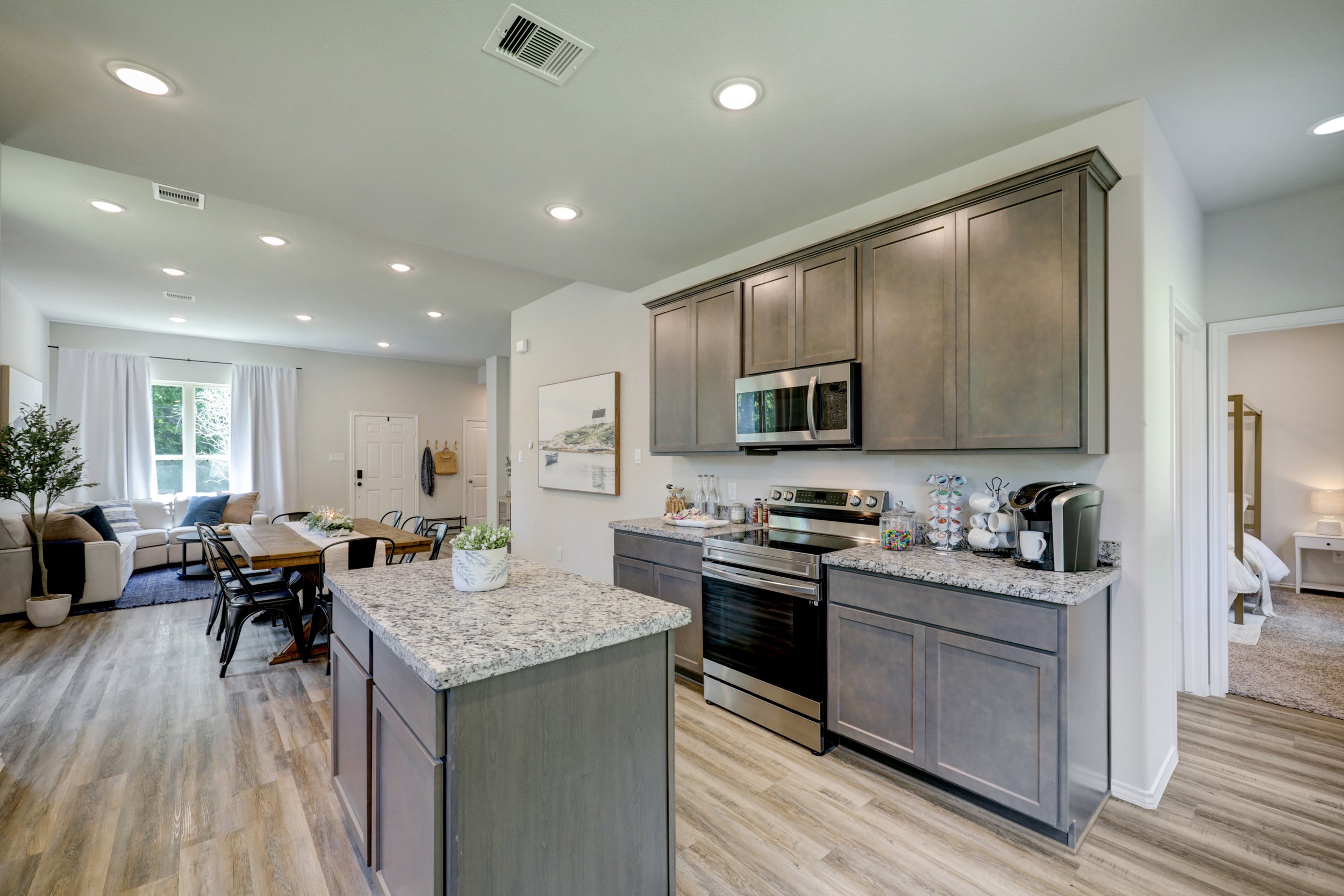 Modern open-concept kitchen with gray cabinets, granite countertops, stainless steel appliances, and adjacent dining and living areas