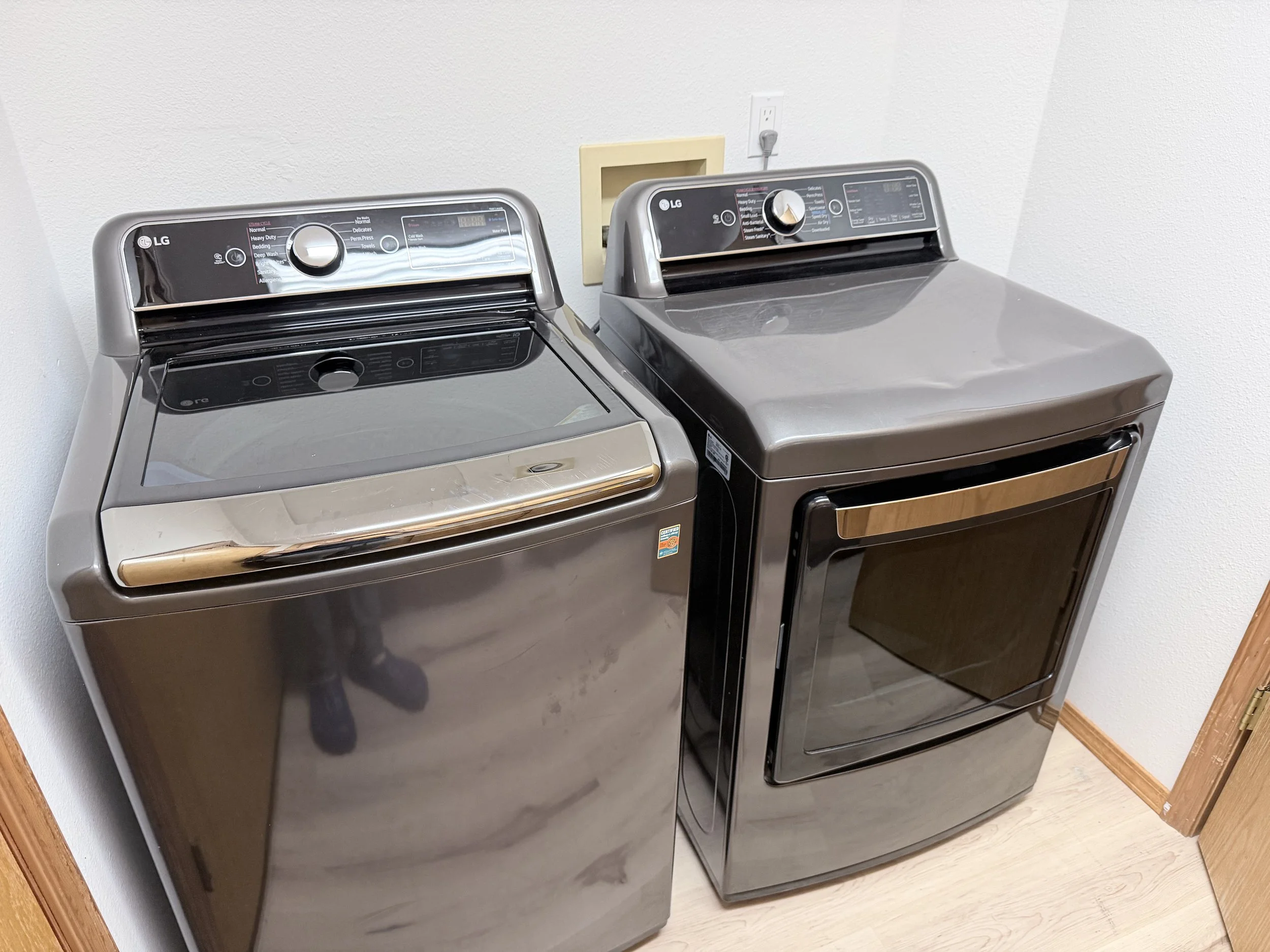 Two gray LG top-load washing machines beside a matching front-load dryer in a laundry room.