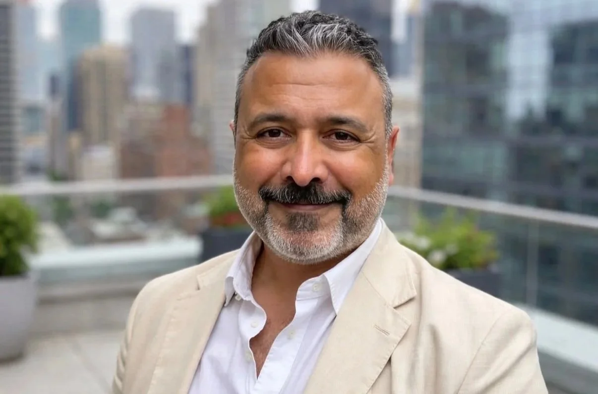 Smiling middle-aged man in a beige blazer standing on a city rooftop