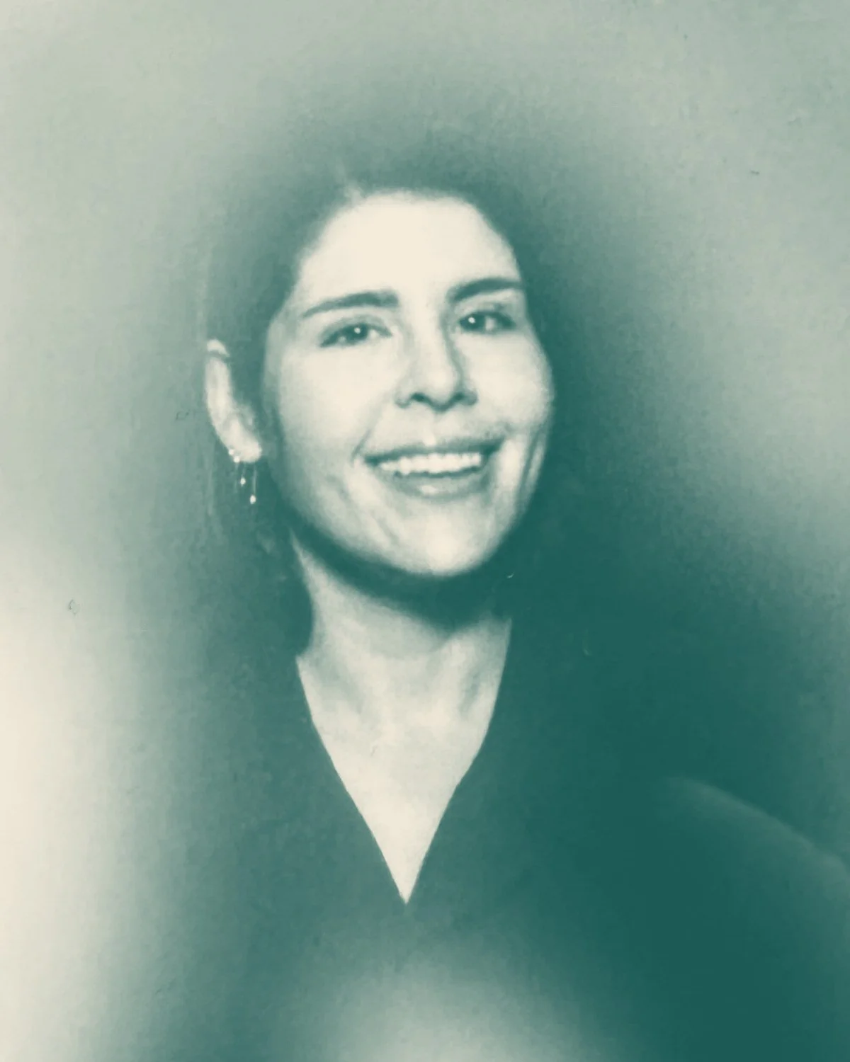 Black and white portrait of a woman smiling, wearing earrings and a dark top, against a dark background.