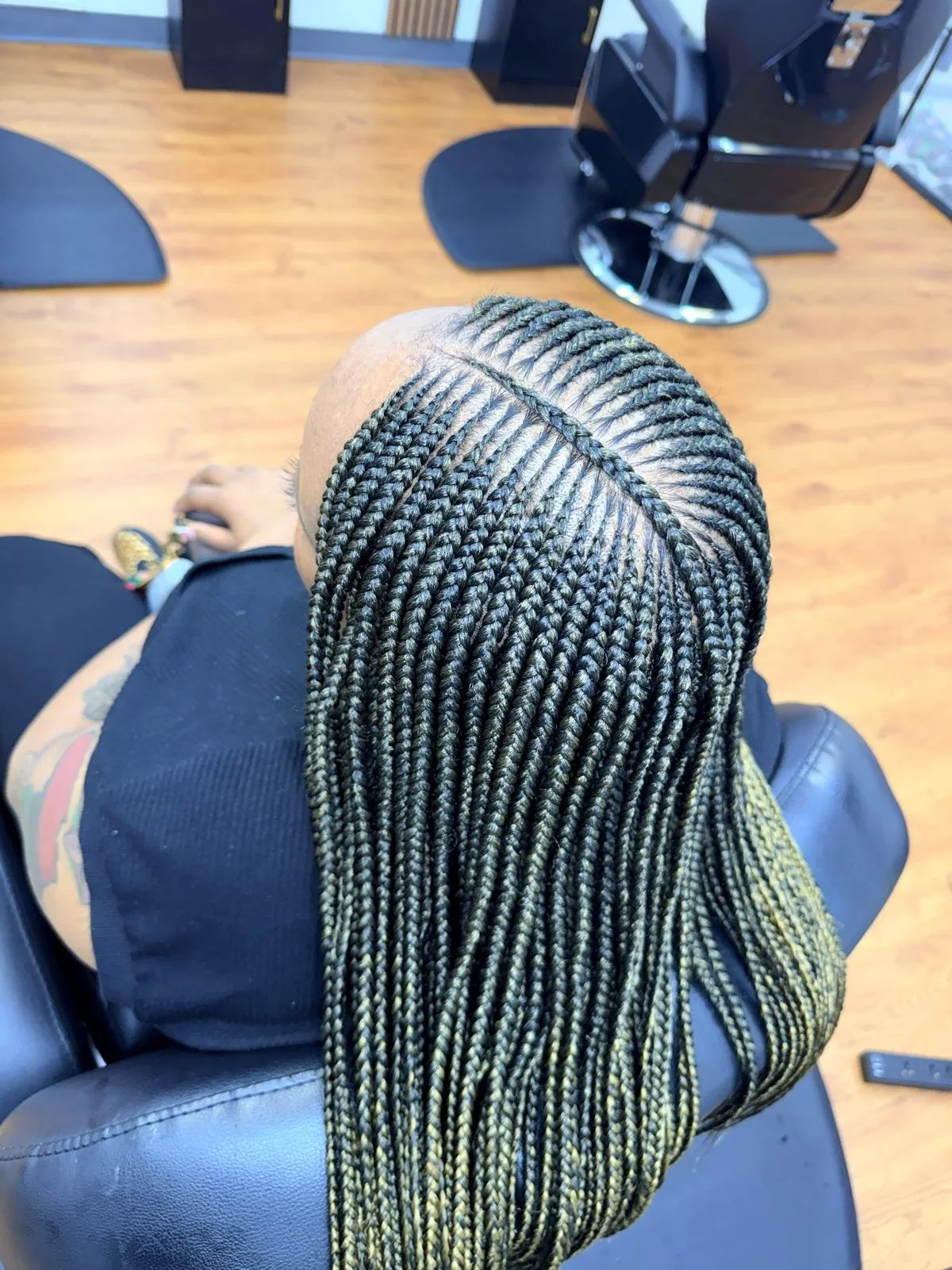 Top view of a person with long, yellow and black box braids sitting in a salon chair.